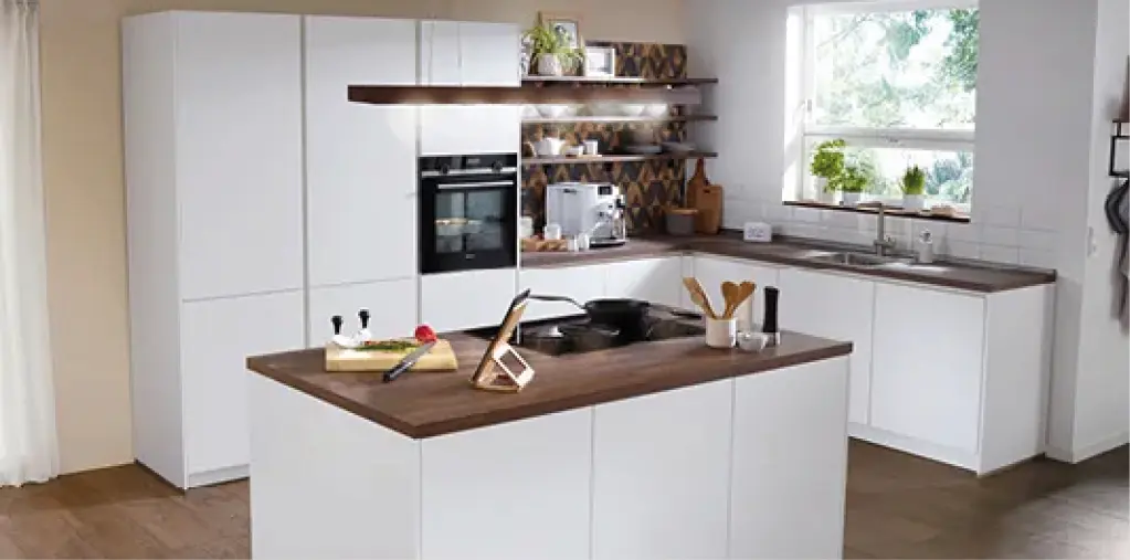 Helle Einbauküche mit Kochinsel, weißen Fronten und Arbeitsplatte in Holzoptik. Offene Küche mit Stauraum, Backofen, Spüle und dekorativen Elementen für modernes und funktionales Küchendesign.